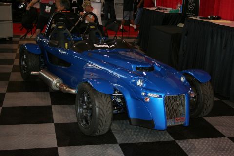 1998 Ford Crown Victoria - blue lightweight roadster-style kit car with exposed wheels sits on a checkered floor at an indoor show.