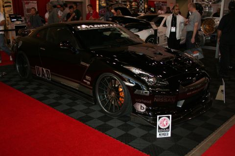 1998 Ford Crown Victoria - black Nissan GT-R R35 with red trim accents and bronze multi-spoke wheels on a red display platform.