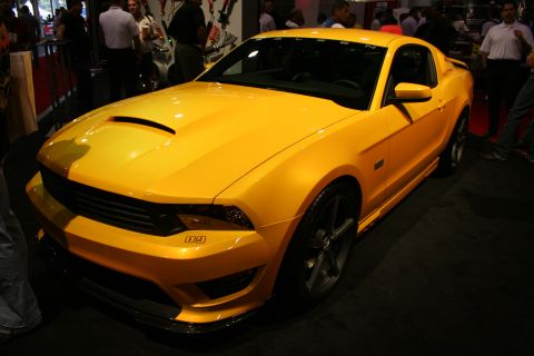 1998 Ford Crown Victoria - yellow Saleen-bodied Ford Mustang shown front three-quarter under show lighting with spectators behind it.