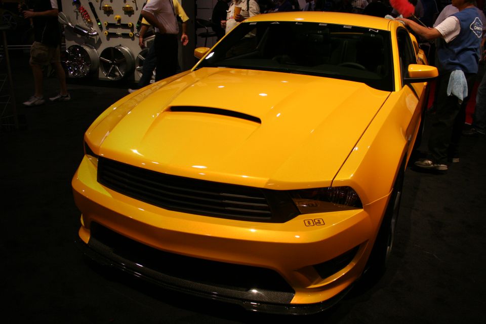 Front view of a yellow Saleen Mustang with hood scoop under show lights
