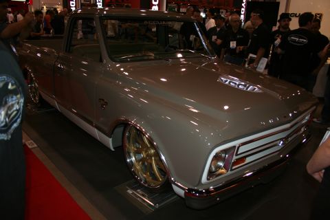 1998 Ford Crown Victoria - lowered gray custom classic Chevrolet C10-style pickup with chrome bumper and gold wheels on a show stand.