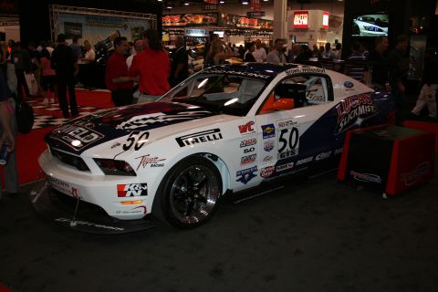 1998 Ford Crown Victoria - white and blue Ford Mustang race car wearing number 50 and numerous sponsor decals on a show floor.