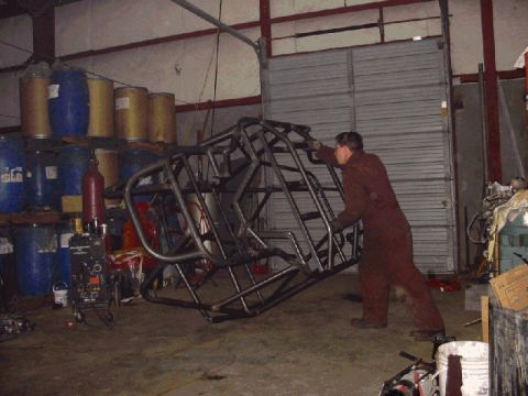 1994 Ford Bronco - A person is moving a metal frame, possibly for a custom vehicle, in a workshop setting.