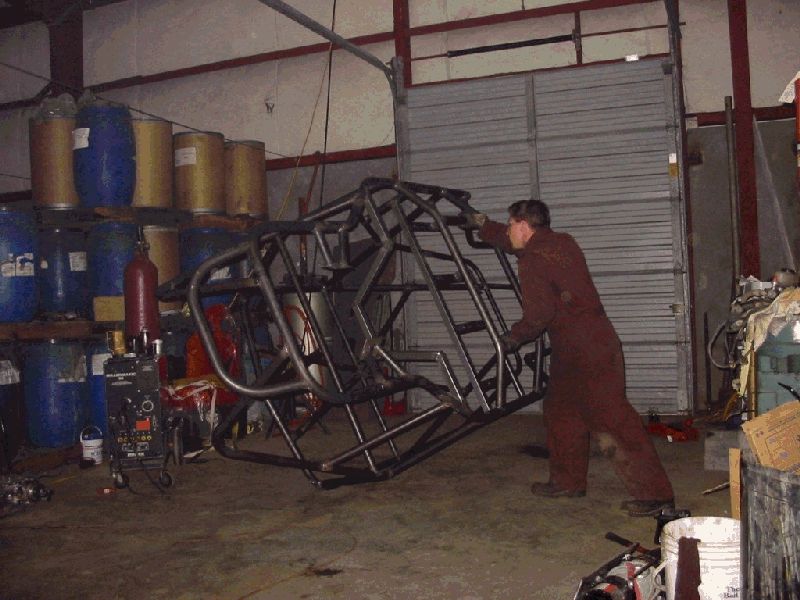 man in jumpsuit moving metal tubing frame in workshop