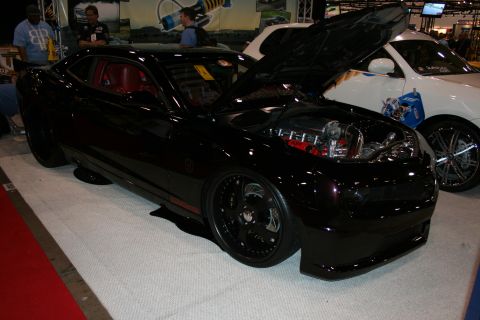 1998 Ford Crown Victoria - blacked-out modern Camaro coupe with a red interior and open hood displayed on a carpeted show stand.