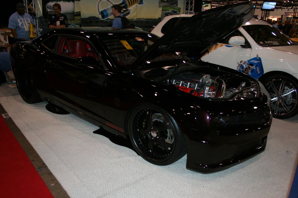 Black modern Camaro with red interior and open hood at a show