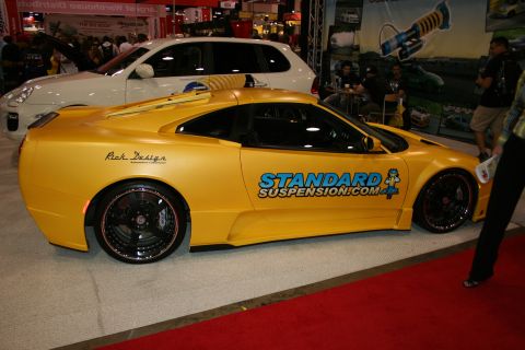 1998 Ford Crown Victoria - Side view of a yellow widebody custom sports car wearing StandardSuspension.com graphics on a show floor.