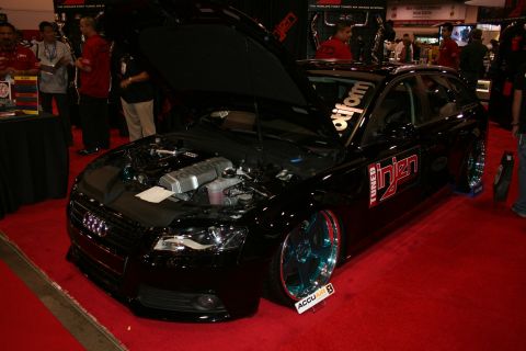 1998 Ford Crown Victoria - lowered black Audi station wagon with the Audi rings, an open hood and turbo-tuner decals on a red carpet.
