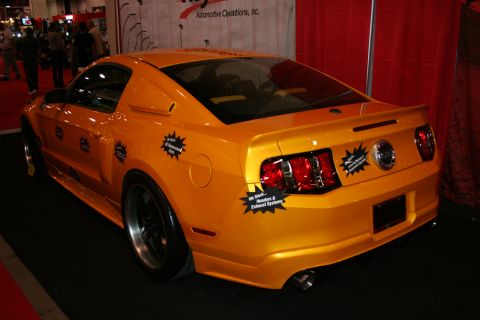1998 Ford Crown Victoria - Rear three-quarter view of an orange sports coupe covered in starburst spec stickers at an indoor trade show booth.