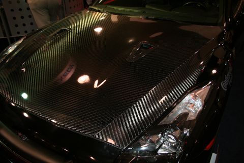 1998 Ford Crown Victoria - Close-up of a glossy carbon-fiber hood and clear headlight assembly on a dark vehicle under show lighting.