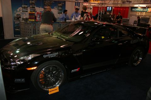 1998 Ford Crown Victoria - black two-door sports coupe covered in sponsor decals sits on display at a busy indoor trade-show booth.