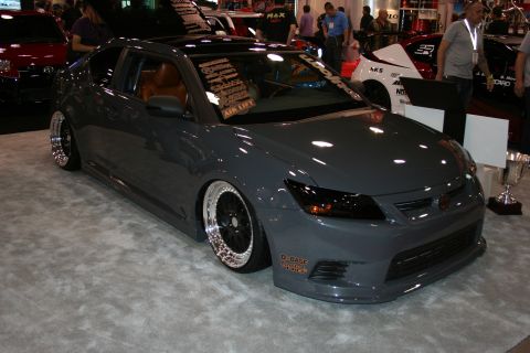 1998 Ford Crown Victoria - Front three-quarter view of a slammed gray sedan with chrome-lipped wheels and a tan interior on a show stand.