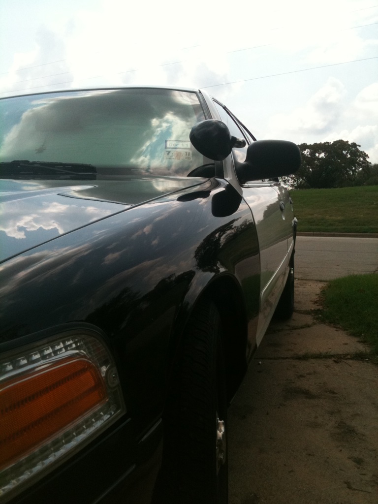 Close-up of front left corner of black-and-white Crown Victoria sedan parked by a grassy roadside