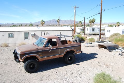 1982 Ford Bronco - This brown Ford Bronco features a roll cage and a spare tire mounted in the bed, seen in a desert landscape.