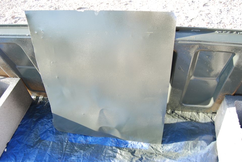 Close-up of a dented, painted car door panel resting on a blue tarp