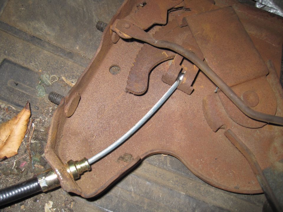Rusted metal bracket with brake cable attached. Bolts visible on bracket
