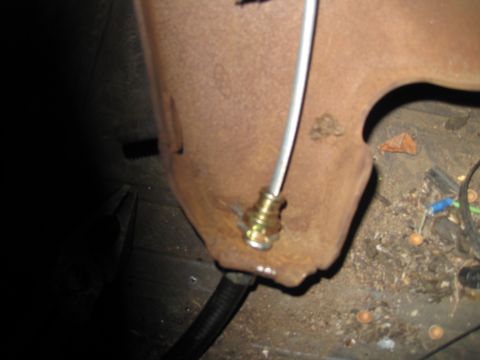 1979 Ford Bronco - Close-up of a brake line fitting attached to a rusty metal panel, with visible debris on the floor.
