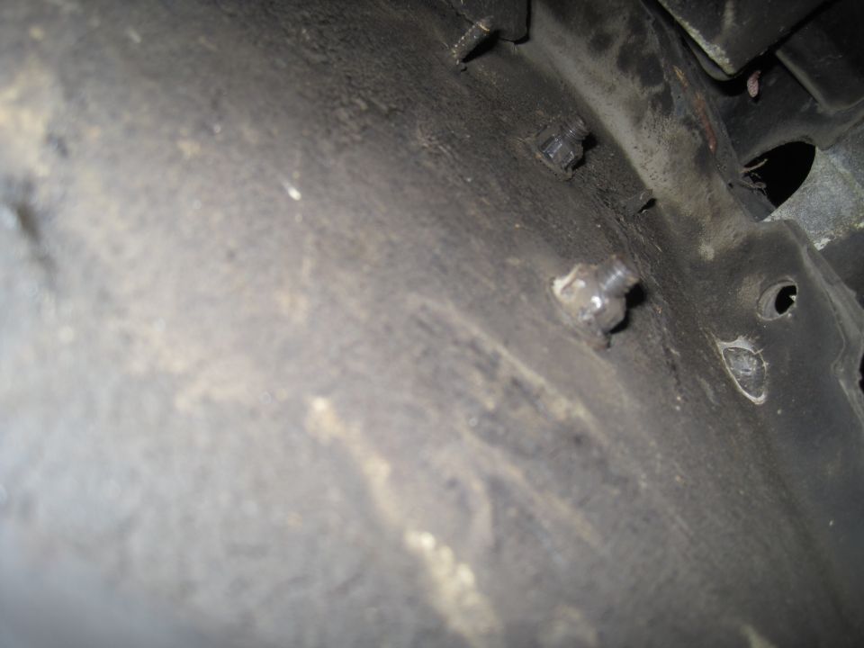 Close-up of rusted bolts on a dark, textured vehicle undercarriage
