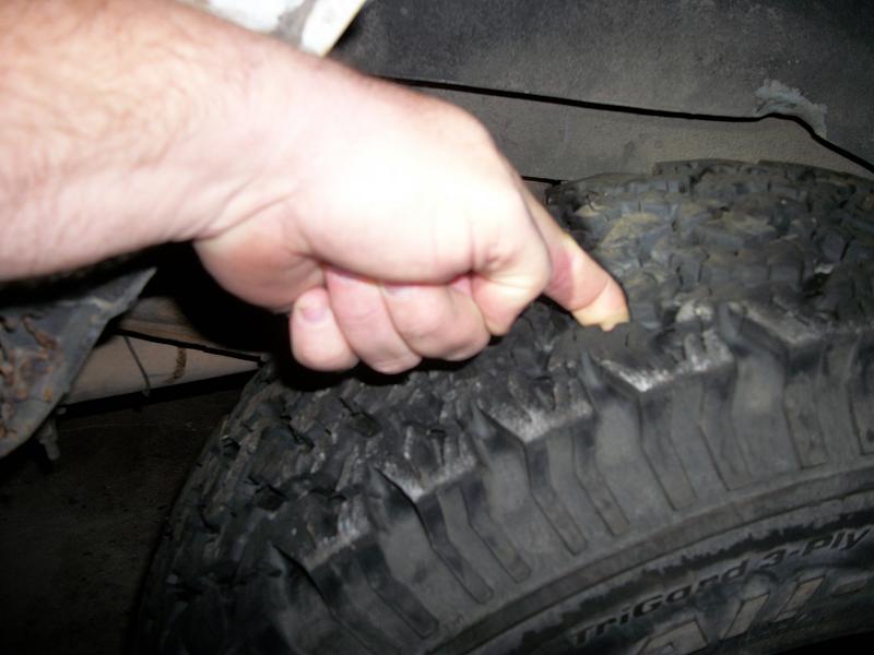 Hand pressing into a worn tire tread. Text on tire is partially visible