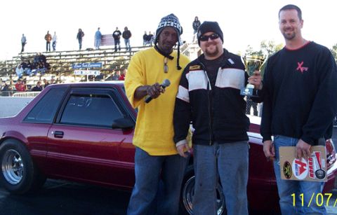 1992 Ford Mustang - Three men pose with a trophy next to a red coupe at a drag racing event.