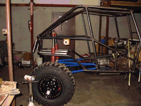 1994 Ford Bronco - The frame of a custom off-road buggy is shown in a workshop setting, a roll cage and heavy-duty suspension.
