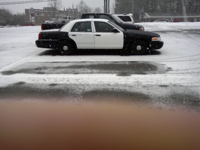 Side view of a two-tone black and white 2003 Ford Crown Victoria police car in snow