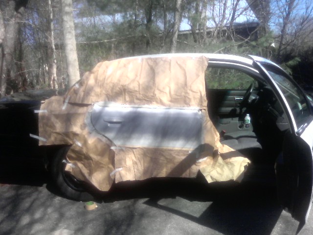 Car door covered in masking paper with primer visible, interior visible through open door