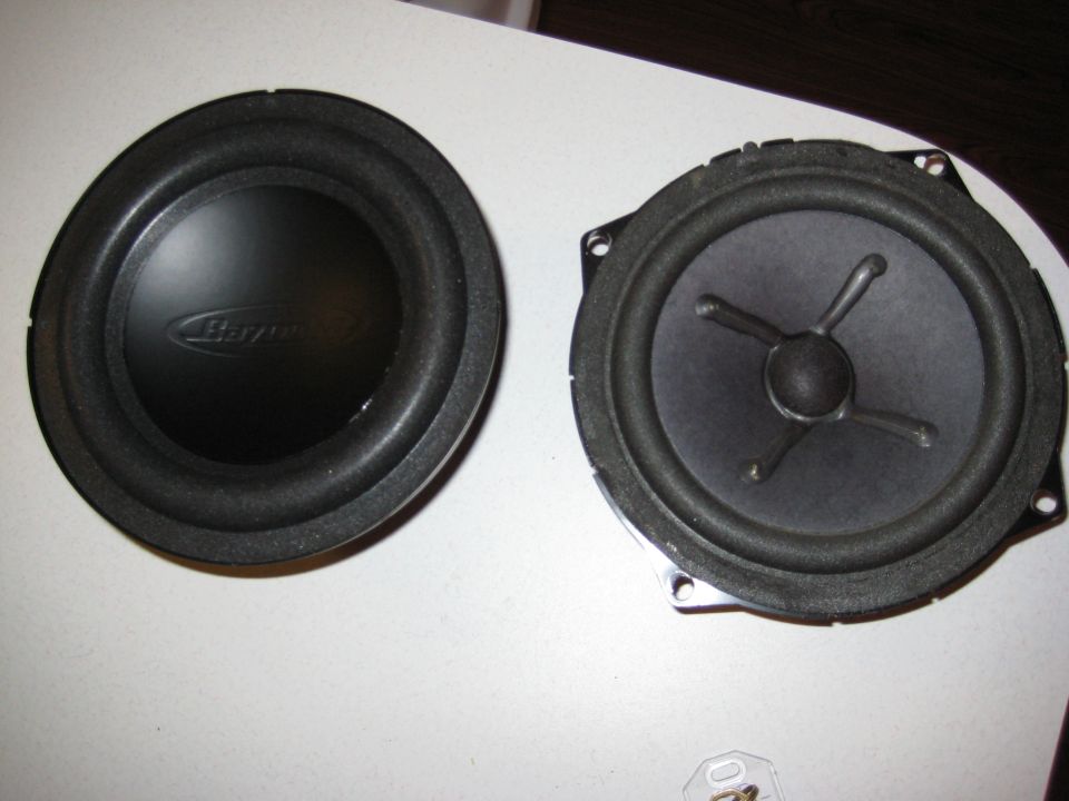 Two black car speakers, one a subwoofer with a 'Basswerk' logo, the other a standard speaker, lie on a white surface