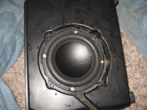 2005 Jeep Wrangler - A Bazooka brand subwoofer is shown installed in its enclosure, with parts of jeans and carpet in the background.