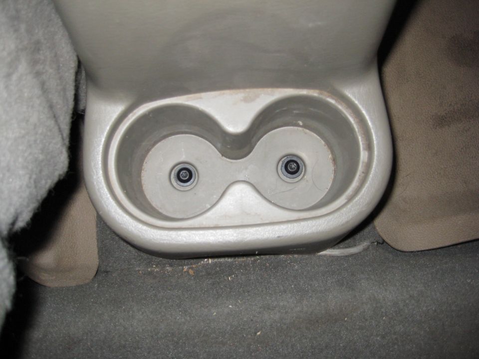 Tan rear center-console dual cup holder with drain grommets, dusty, in a vehicle interior
