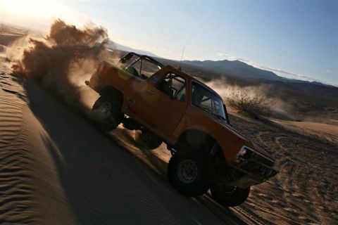 1986 Ford Bronco - Off-road Bronco navigates a steep sand dune, creating a dust cloud.
