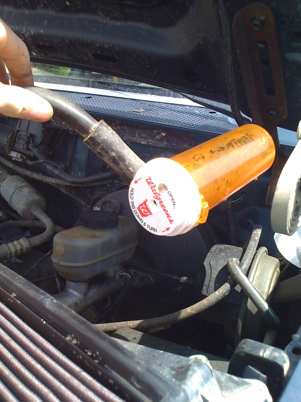 Engine bay with a pill bottle cap used as a temporary fix on a hose