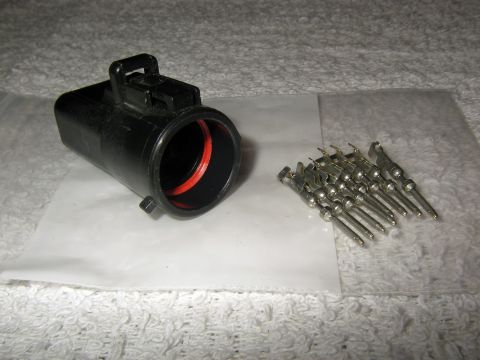 1990 Ford Bronco - A black electrical connector housing and a group of metal pins are laid out on a white surface.