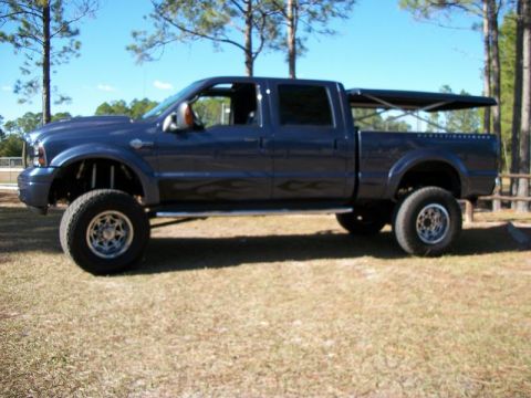 1992 Jeep Cherokee - This lifted crew cab pickup truck is shown from the side on a grassy field under a clear blue sky.
