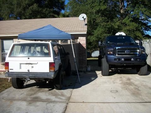 1992 Jeep Cherokee - A white 1992 Jeep Cherokee is seen from the rear, parked next to a blue Ford F-Series truck.