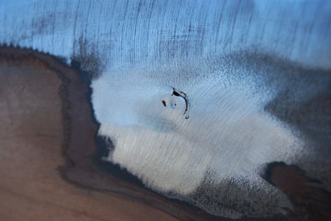 1982 Ford Bronco - Close-up of a metal body panel undergoing repair, revealing primer and filler work on a dent.