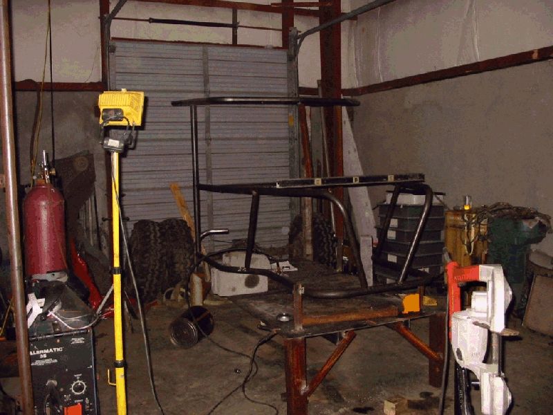 Early tube chassis tacked on a welding table with a level clamped across it, welder nearby