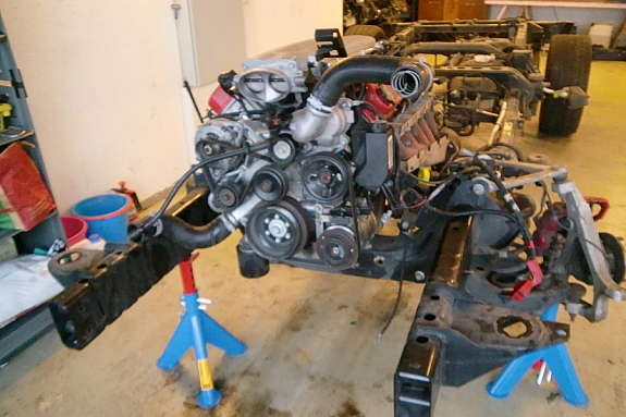 Engine and chassis assembly on jack stands, with visible hoses and belts
