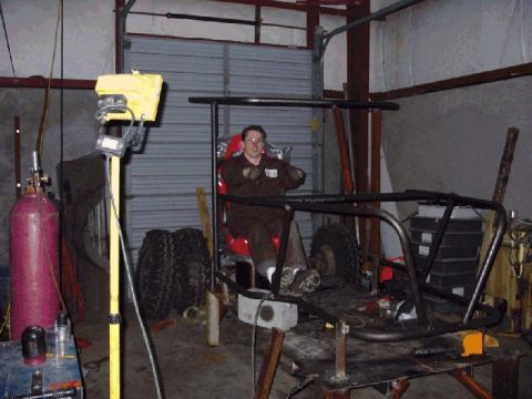 1994 Ford Bronco - A person sits in a custom-built buggy frame inside a workshop, with tools and tires visible.