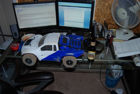 1982 Ford Bronco - A white and blue remote control truck sits on a desk next to computer monitors and a beer bottle.