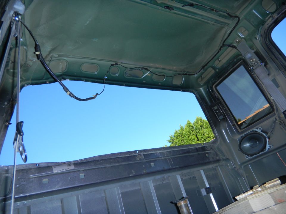 Interior of a green truck cab, looking out the open roof and rear window at a blue sky and trees