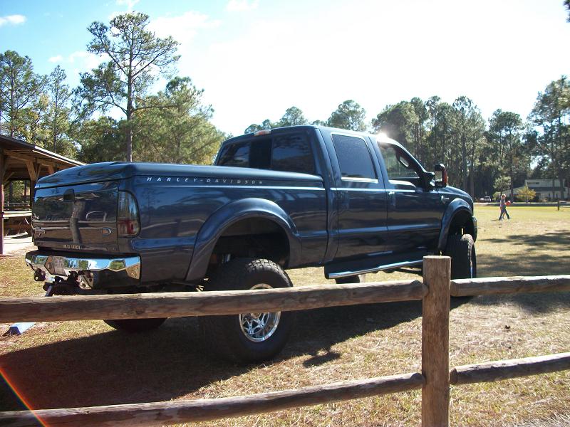 Blue Ford F-Series Super Duty truck with Harley-Davidson badging on the bed cover, lifted with large tires
