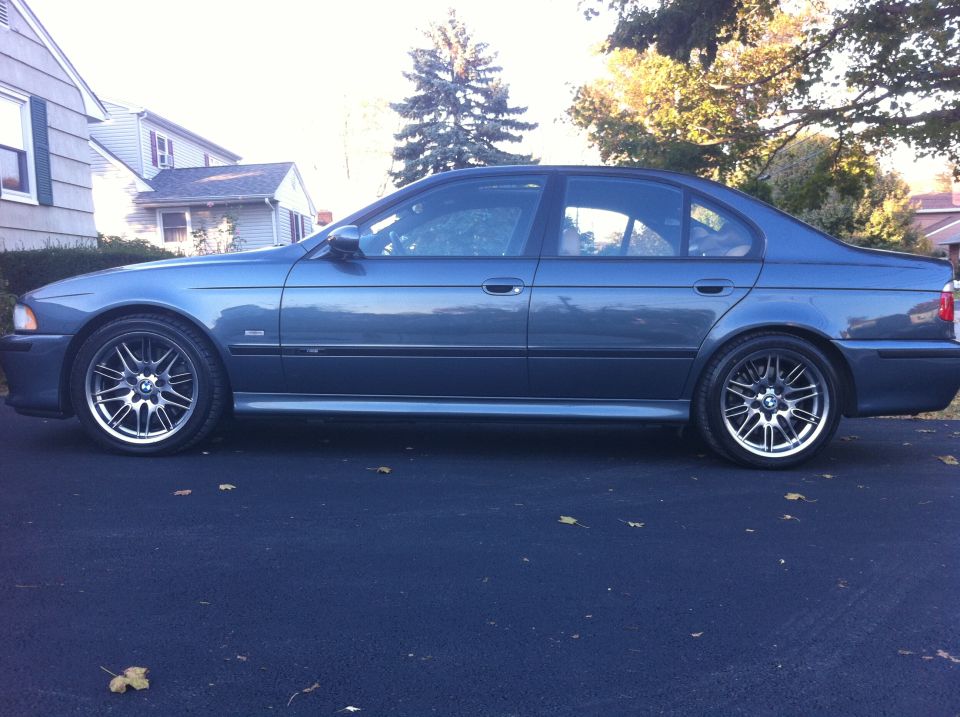 Blue-gray BMW E39 5 Series sedan side profile on suburban street with M-style wheels