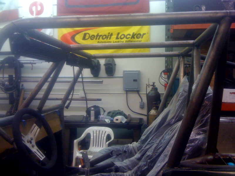 Custom roll cage structure in a workshop with a Detroit Locker banner in the background
