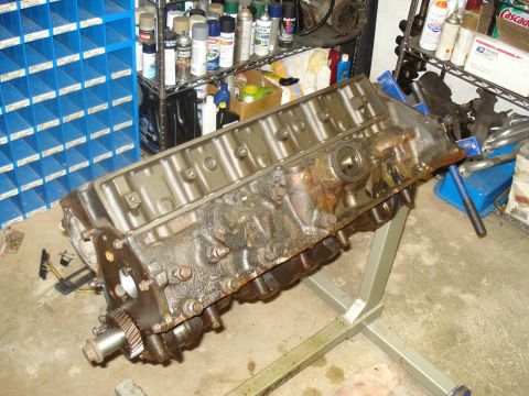 1991 Ford Bronco - An engine block is displayed on a stand in a workshop environment, with various automotive supplies in the background.