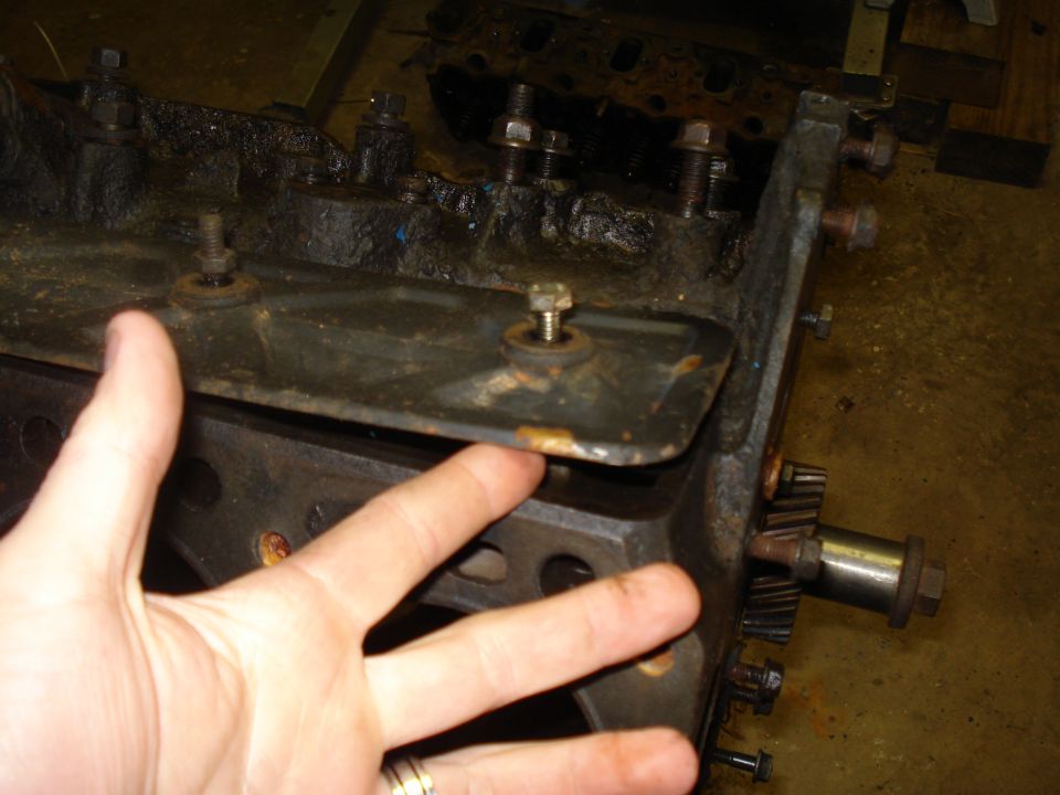 Close-up of an engine block with gears visible, a hand is pointing to a metal plate