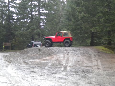2005 Jeep Wrangler - A red Jeep Wrangler is parked on a dirt incline with a tan soft top, accompanied by another vehicle in the background.