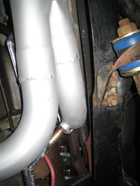 1996 Ford Bronco - Close-up view of exhaust manifold pipes and an oxygen sensor, with a suspension component visible in the background.