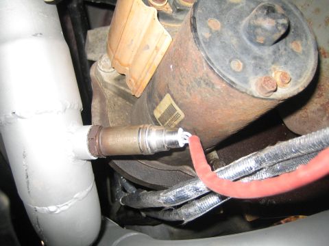 1996 Ford Bronco - Close-up of an exhaust system part, likely an oxygen sensor, connected to a vehicle's undercarriage.