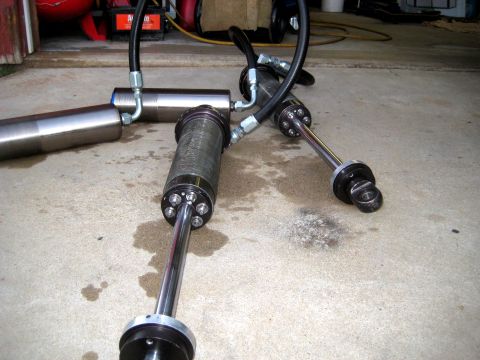1996 Ford Bronco - Three hydraulic shock absorbers with hoses are laid out on a concrete floor.